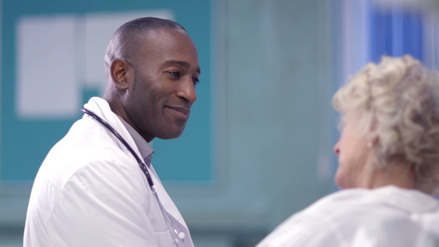Caring doctor chats with an elderly female patient on a hospital ward.