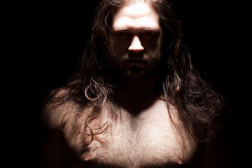 Very big guy with long hair an angry face on black background