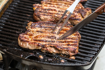 Beef steaks on grill with BBQ fork and knife