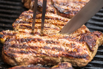 Beef steaks on grill with BBQ fork and knife