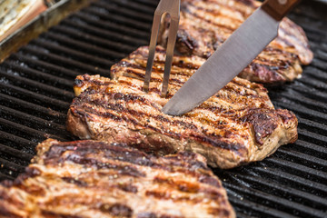 Beef steaks on grill with BBQ fork and knife