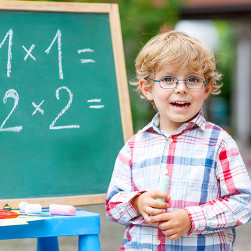Cute little kid boy with glasses at blackboard practicing mathem