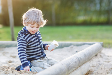 Adorable toddler boy having fun with sand on outdoor playground