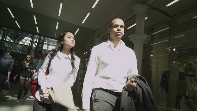 Young professional man & woman chat as they walk through London railway station
