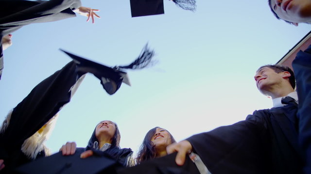Happy multi-ethnic friends on graduation day throw their caps into the air