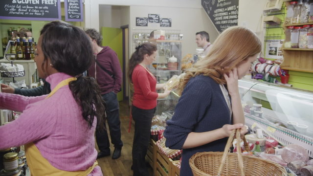 Employees working and shoppers browsing in a local delicatessen or food store.