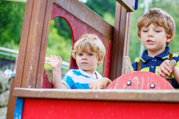 Two kid boys pretends driving an imaginary car on playground,