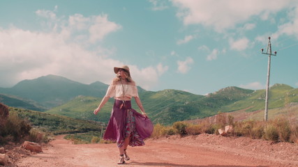 Rearview of boho girl walking down a country dirt road