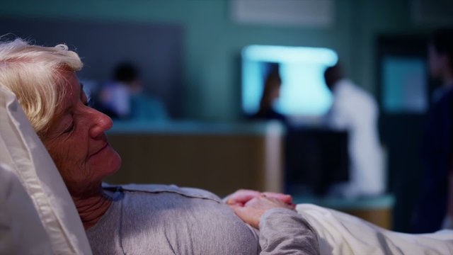Elderly female patient resting in bed with medical team working in the background