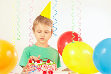 Fototapeta na wymiar Little kid in festive hat looking at the birthday cake