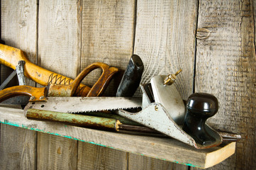 Many old tools ( axe, saw and others) on a wooden shelf.