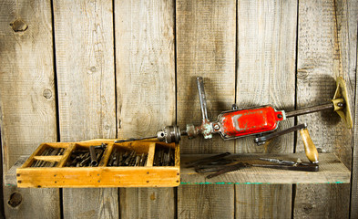 Many old tools ( drill, pliers and others) on a wooden shelf.