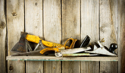 Many old tools ( axe, saw and others) on a wooden shelf.