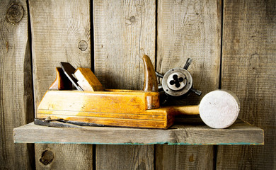 Many old tools ( plane, mallet and others) on a wooden shelf.