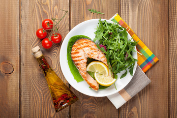 Grilled salmon, salad and condiments on wooden table