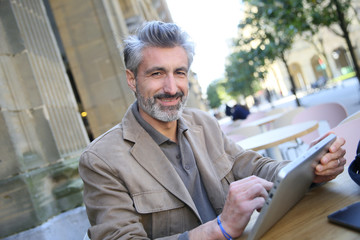 Mature man in town using tablet at coffee shop
