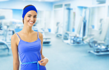 Woman in sportswear measuring waist, at gym