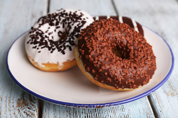 Delicious donuts with icing on plate on wooden background