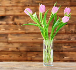 Beautiful pink tulips in vase on table on wooden background