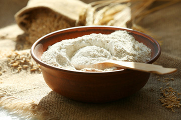 Bowl of flour with wooden spoon on burlap cloth background