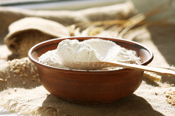 Bowl of flour with wooden spoon on burlap cloth background