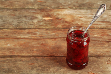 Jar of strawberry jam with spoon on wooden background