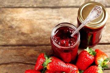 Jars of strawberry jam with berries on wooden background