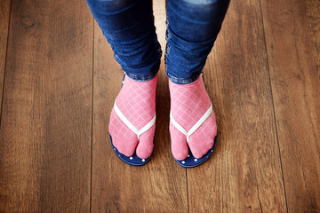 Female feet in socks with pink flip-flops, on floor background