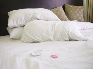 Messy bed in a hotel with a pink condom