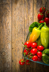 Red tomato, yellow pepper and green salad on wooden table.
