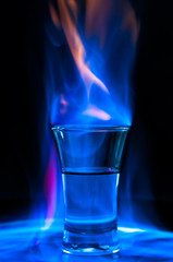 Glass with burning alcohol on black background