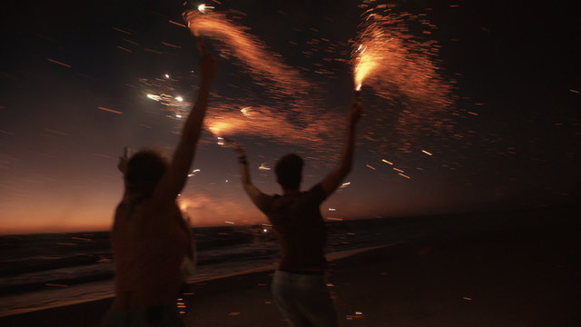 Friends running on a beach with fireworks