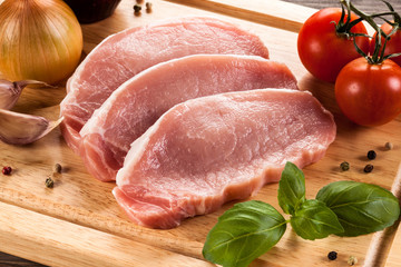 Raw pork chops on cutting board and vegetables