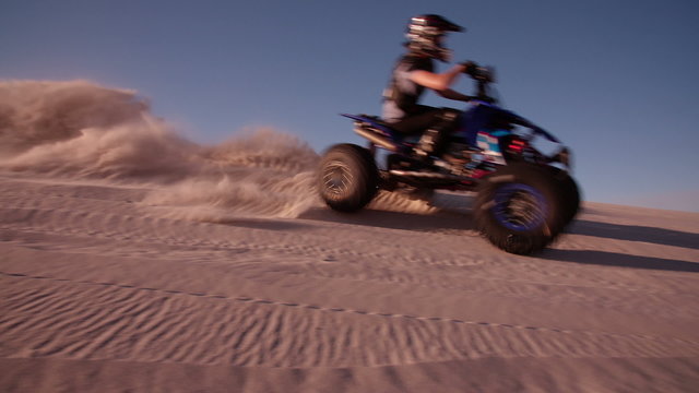 Quad racer driving up a sand dune with sun flare
