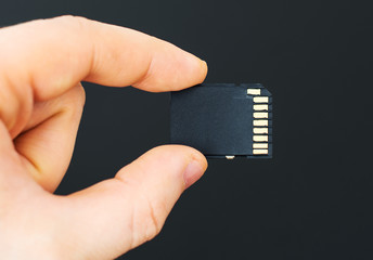 Male hand holding SD card on black background.