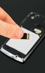 Male hand holding Micro SD card near mobile phone.