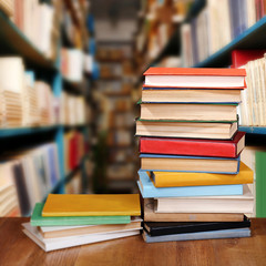 Stack of books on table on bookshelves background