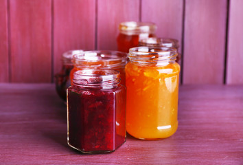Homemade jars of fruits jam on color wooden background