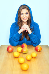 Smiling woman sitting at the wooden table with fruit.