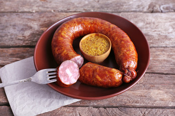 Smoked sausage with mustard on plate on wooden table background