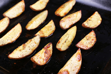 Baked potatoes with spices on pan close up