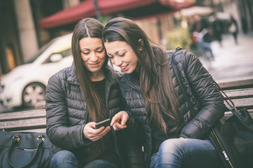 Two female twins looking at a smart phone - obrazy, fototapety, plakaty