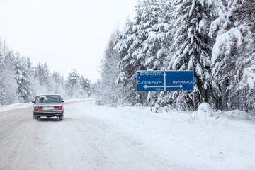 Car drives near roadsign with directions to highway in winter