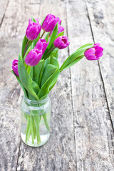 bouquet of violet tulips on the oak brown table in a glass jar