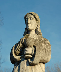 Fototapeta na wymiar Old stone statue of a woman with a cup for Holy Communion on the