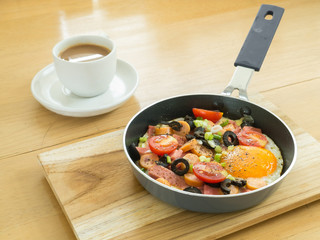 Fried egg with sausage in a pan and  hot coffee on wooden table