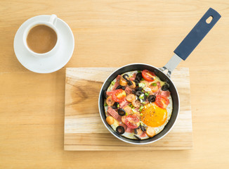 Fried egg with sausage in a pan and  hot coffee on wooden table