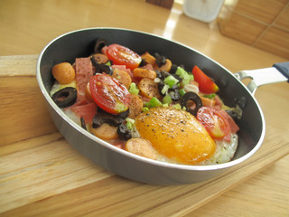 Fried egg with sausage ,tomatoes and olives in a pan on wooden t