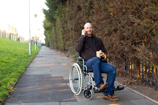 Young Man In A Wheelchair Talking On The Phone With A Coffee