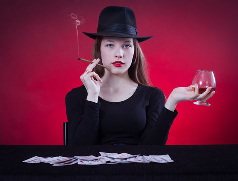 woman playing cards sitting at the table and smoking a cigar.